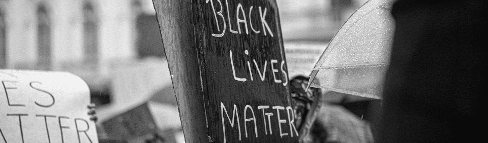 A grayscale image of a protest with a sign that reads "Black Lives Matter" as the focal point